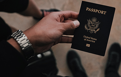 picture of a hand of a person with brown skin wearing a silver watch band holding a US passport
